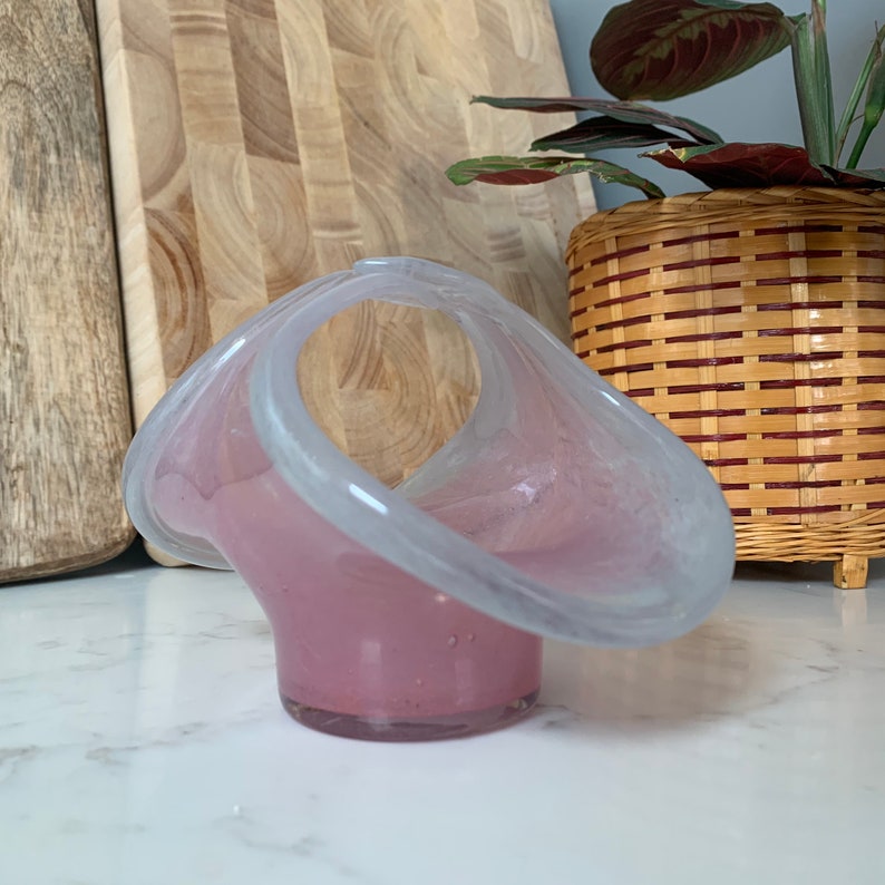May include: A pink and white glass bowl with a unique, wavy design. The bowl has a handle and is perfect for holding small items.