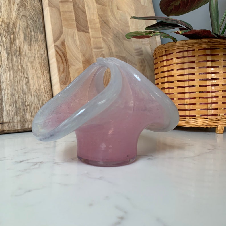 May include: A white and pink glass vase with a unique, organic shape. The vase has a wide opening and a narrow base.