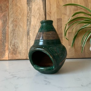 May include: Green ceramic ashtray with a carved design. The ashtray has a wide opening and a rounded base.
