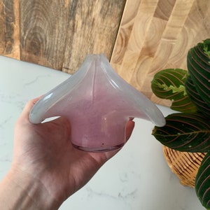 May include: A small, pink and white glass vase with a unique, flower-like design. The vase has a wide, open top and a narrow base.