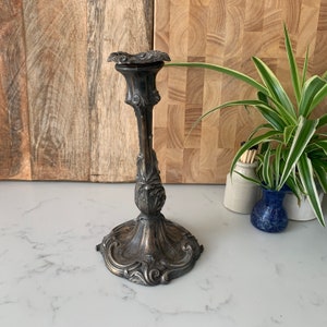 May include: A silver candlestick with an ornate design. The candlestick has a round base with intricate details and a tall, slender stem.
