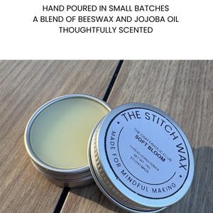 May include: A round silver metal tin containing light yellow thread conditioner wax. The lid is labeled THE STITCH WAX, THE CRAFTAHOLIC CLUB SOFT BLOOM, THREAD CONDITIONER, NET WT. 14G, STUDIO MADE, MADE FOR MINDFUL MAKING. Text above reads MADE FOR MINDFUL MAKERS.