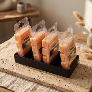May include: A black rectangular organizer holds five individually packaged, light orange wax melts. Each melt is in a clear plastic clamshell with a label. The organizer sits on a light-colored stone surface.