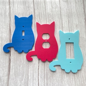 May include: Three cat-shaped light switch covers in blue, red, and light blue. The covers are made of a thick, durable material and have a smooth, glossy finish.