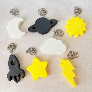 May include: A set of three ceramic mugs with a speckled, matte finish. The mugs are in shades of cream, light gray, and dark gray. Each mug has a simple, minimalist design and a rounded handle.