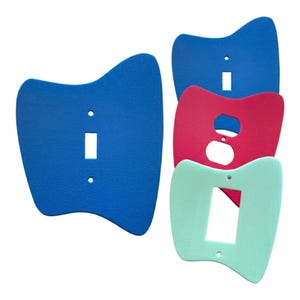 May include: A collection of colorful light switch covers in blue, red, and mint green. Each cover has a unique, curved shape and cutouts for switches and outlets. The covers are made of a textured material.