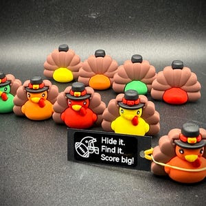 May include: A group of colourful turkey-shaped charms, each with a brown fan, a black hat, and a different coloured body. A small black sign reads "Hide it. Find it. Score big!" These charms are likely for a holiday or seasonal theme.