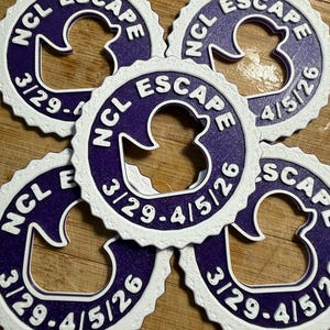 May include: Five circular purple and white plastic tags with a scalloped edge. Each tag features a central cutout in the shape of a rubber duck, with the text NCL ESCAPE and the date range 3/29-4/5/26 embossed in white on the purple surface.