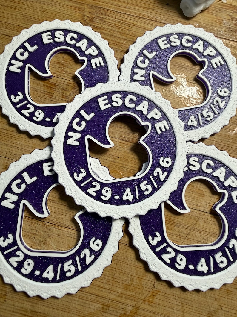 May include: Five circular purple and white plastic tags with a scalloped edge. Each tag features a central cutout in the shape of a rubber duck, with the text NCL ESCAPE and the date range 3/29-4/5/26 embossed in white on the purple surface.
