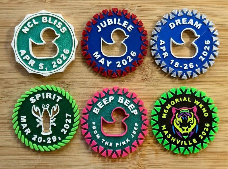 May include: Six circular 3D-printed cruise ship tags featuring various icons like ducks, a lobster, and a tiger. Each tag displays specific text including NCL BLISS APR 5 2026, JUBILEE MAY 2026, DREAM APR 18-26 2026, SPIRIT MAR 20-29 2027, BEEP BEEP FROM THE PINK JEEF, and MEMORIAL WKND NASHVILLE 2026.