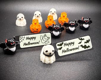 May include: A collection of Halloween-themed figurines, including ghosts, bats, and jack-o'-lanterns. The figurines are in various poses and colors, with the text "Happy Halloween!" on small signs. The overall theme is festive and spooky.