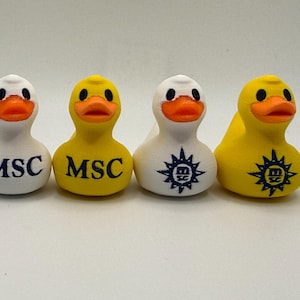 Op de afbeelding: Vier rubberen badeenden, twee witte en twee gele, met oranje snavels. De witte eenden hebben de letters "MSC" in marineblauw gedrukt, en de andere twee hebben een marineblauw logo. De gele eenden hebben ook de letters "MSC" in marineblauw.