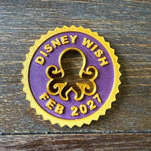 May include: A circular medallion with a serrated gold edge and a purple center. The text "DISNEY WISH" is embossed in gold at the top, and "FEB 2027" is embossed in gold at the bottom. A gold octopus silhouette is centered in the middle.