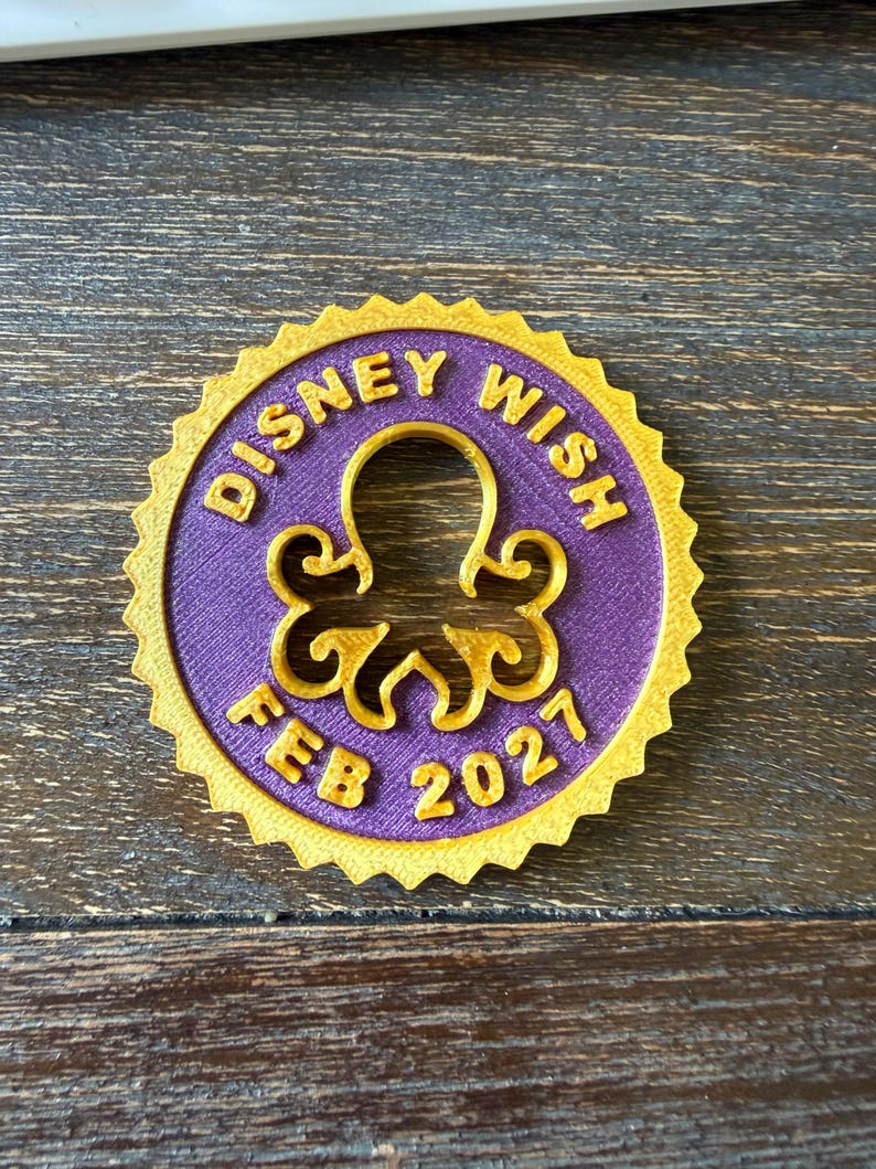 May include: A circular medallion with a serrated gold edge and a purple center. The text "DISNEY WISH" is embossed in gold at the top, and "FEB 2027" is embossed in gold at the bottom. A gold octopus silhouette is centered in the middle.