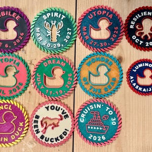 May include: Eleven circular 3D-printed cruise ship duck tags with rope-textured borders. Each tag features unique text and icons, including ducks, a lobster, a horse, and a cruise ship, with various dates and ship names like Jubilee, Spirit, and Utopia.