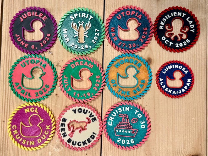 May include: Eleven circular 3D-printed cruise ship duck tags with rope-textured borders. Each tag features unique text and icons, including ducks, a lobster, a horse, and a cruise ship, with various dates and ship names like Jubilee, Spirit, and Utopia.