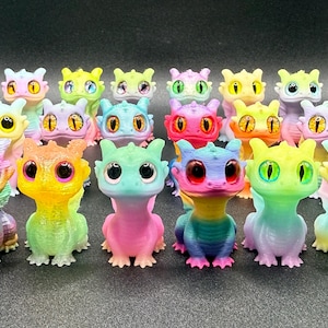 May include: A group of small dragon figurines in various colours. Each dragon has large eyes and is painted in a gradient of colours, including pink, blue, yellow, and green. The dragons are arranged on a dark surface.