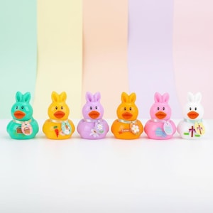 May include: A row of six brightly coloured Easter-themed rubber duck toys. Each duck has bunny ears and a decorative scarf. The ducks are in shades of green, yellow, purple, orange, pink, and white, with various Easter-related embellishments.