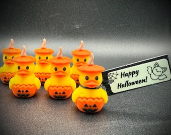 May include: A collection of yellow and orange Halloween duck figurines, each with a pumpkin-shaped body and a matching hat. A small sign with the words "Happy Halloween!" and a bat illustration is also present.
