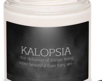 Pode incluir: Uma vela branca acesa em um frasco de vidro transparente com um rótulo preto. O rótulo diz "KALOPSIA - a ilusão de que as coisas são mais bonitas do que são". Uma tampa preta está ao lado do frasco. A vela é um item de decoração.