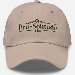 May include: A tan baseball cap with the text "Pro-Solitude" in dark green. The text is above a mountain graphic and two small trees. The cap has a curved brim and a button on top.
