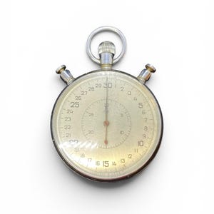May include: A silver-toned analog stopwatch with a circular face, featuring a main dial marked from 1 to 30 and an inner sub-dial marked from 5 to 25. The device includes a top winding crown with a ring and two side push buttons for operation.