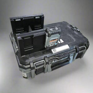 May include: A black and gray Stack Pack tool storage box with a black accessory and a battery pack. The box has a handle and latches. The battery pack has a label with text. The accessory is open.