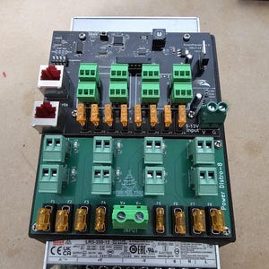 May include: A black and green electronic device with the text "Power Distro-8" printed on the side. The device has multiple green and black connectors and a label that reads "LRS-350-12".