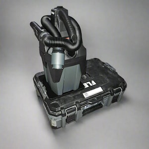 May include: A black and gray vacuum cleaner with a hose and a handle. The vacuum cleaner is sitting in a black toolbox with the word "FLE" printed on the side.