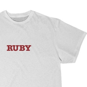 Puede incluir: Camiseta blanca con la palabra "RUBY" impresa en rojo en la parte delantera.