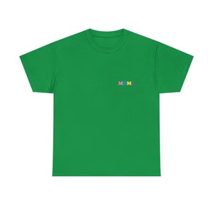 Op de afbeelding: Een groen T-shirt met korte mouwen met het woord "MOMA" geborduurd op de borst in kleurrijke letters.