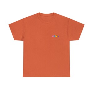 Op de afbeelding: Een oranje T-shirt met het woord "MOMA" geborduurd op de voorkant in kleurrijke letters.