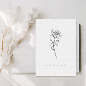 May include: A simple black and white drawing of a rose with the text "our moment" below it. The drawing is on a white card.