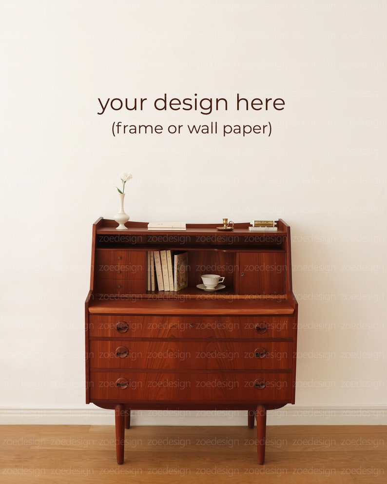 May include: A wooden desk with a drop-down front and three drawers. The desk has a light wood finish and is sitting on a light wood floor. There is a white wall behind the desk. The text "your design here (frame or wall paper)" is written on the wall.