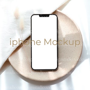 May include: A white smartphone mockup on a beige plate with a white cloth and dried flowers in the background.