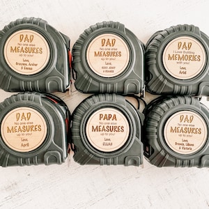 May include: Six black tape measures with wooden labels that say "Dad" or "Papa" and include the text "No one else measures up to you!" with a personalized message of love from family members.