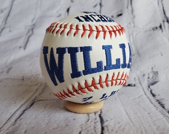 May include: White baseball with red stitching and blue embroidered text "WILLIA" on the side.