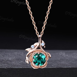 May include: A rose gold necklace featuring a green emerald gemstone set in a rose-shaped pendant. The pendant is accented with two smaller clear gemstones.
