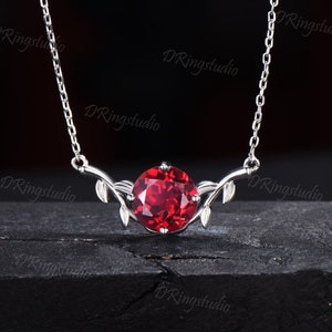 May include: A silver necklace with a red gemstone pendant. The pendant is surrounded by delicate silver leaves.