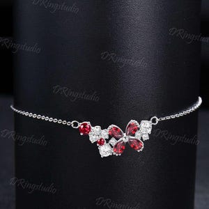 May include: A silver chain necklace with a red and white butterfly pendant. The butterfly is made of cubic zirconia stones and has a delicate design.
