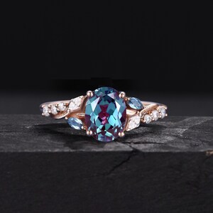 May include: A rose gold ring with an oval-shaped alexandrite gemstone surrounded by smaller diamonds and blue topaz stones. The ring features a delicate, leaf-like design.