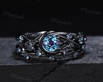 Pode incluir: Conjunto de anéis pretos com uma grande pedra preciosa azul e roxa cercada por pequenas pedras preciosas transparentes. O anel apresenta um design de lua crescente e detalhes florais intrincados.