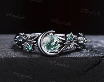 Könnte beinhalten: Ein schwarzer Ring mit einem Halbmond-Design und einem grünen Moosachat-Edelstein. Der Ring ist mit kleinen grünen Sternen und Blättern verziert.