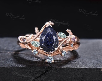 Puede incluir: Un anillo de piedra preciosa azul en forma de pera engastado en oro rosa con un delicado diseño floral. El anillo presenta una banda con piedras preciosas más pequeñas y un diseño de hojas.