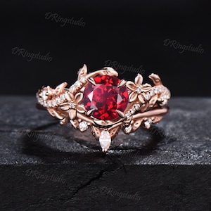 May include: A rose gold engagement ring with a large red gemstone surrounded by smaller white gemstones. The ring features a delicate floral design with leaves and flowers.
