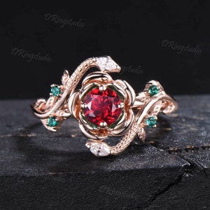 May include: A rose gold ring with a red gemstone surrounded by smaller white gemstones. The ring features a snake design with green gemstones on the band.