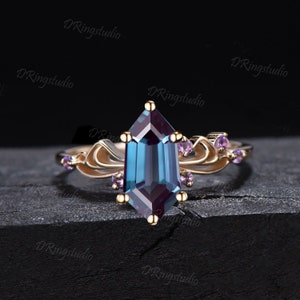 Op de afbeelding: Een gouden ring met een grote, gefacetteerde, blauwgroene edelsteen in een zeshoekige vorm. De ring heeft een delicaat, bloemig ontwerp met kleinere paarse edelstenen.