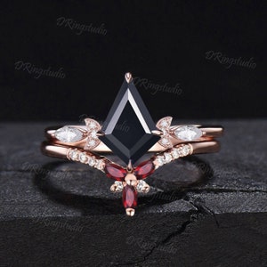 May include: A rose gold engagement ring set with a black square-shaped diamond and a matching band with smaller diamonds and red gemstones.