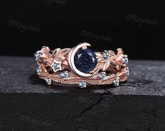 Puede incluir: Un anillo de oro rosa engastado con una piedra preciosa azul y un diseño de luna creciente. El anillo está adornado con piedras azules más pequeñas y un diseño de estrella.