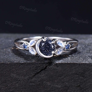 May include: A silver ring with a crescent moon design, a blue star, and a blue gemstone. The ring is set with a blue gemstone in the center, surrounded by a crescent moon and a star.
